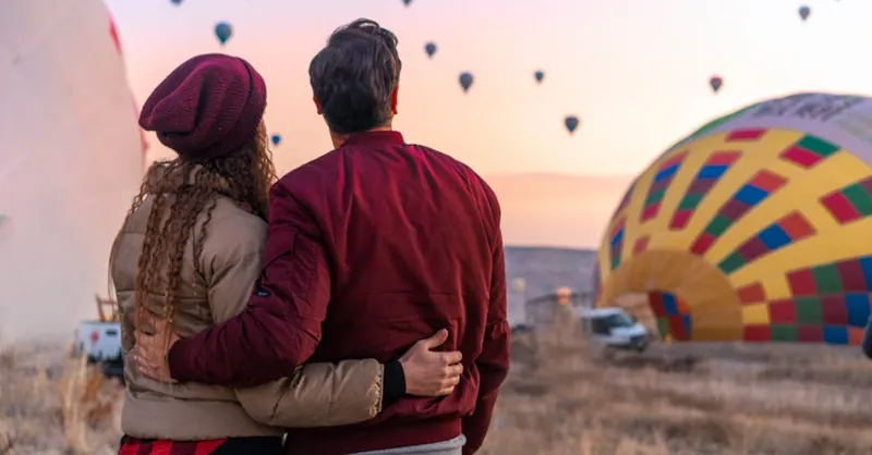 A couple embraces while watching hot air balloons during a colorful sunrise in Cappadocia, Turkey.