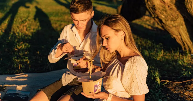Couple enjoying a cozy picnic outdoors during sunset in a serene park setting.