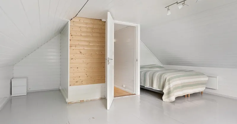 Modern attic bedroom with white walls, wooden accents, and cozy bed in minimalistic style.