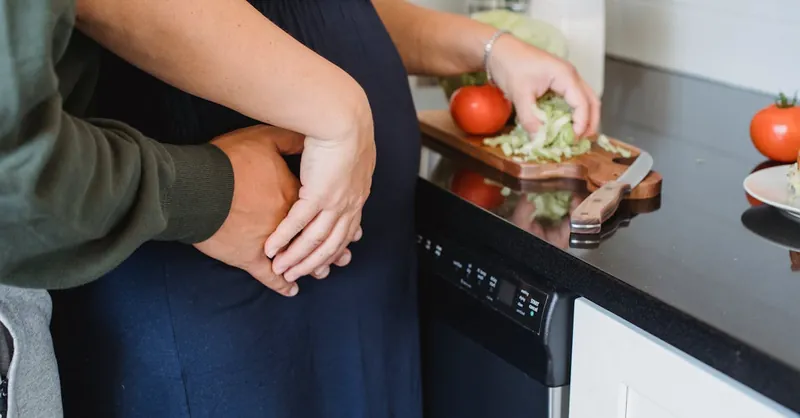 A couple embraces in the kitchen while preparing a fresh salad, symbolizing love and healthy living.