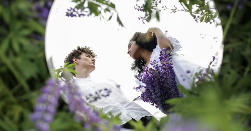 A diverse couple reflected in a mirror surrounded by lupine flowers, symbolizing unity and nature.
