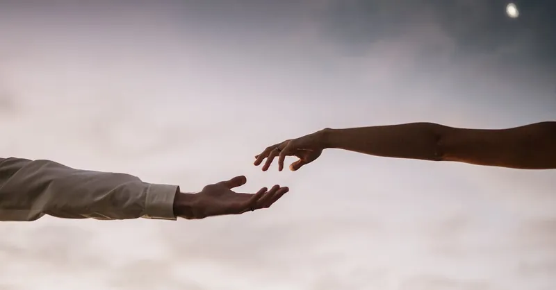 Two hands reaching towards each other against a soft twilight sky symbolizing connection and love.