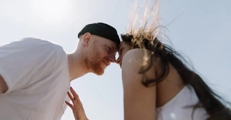 A romantic couple enjoys an intimate moment outdoors, under a clear sky.