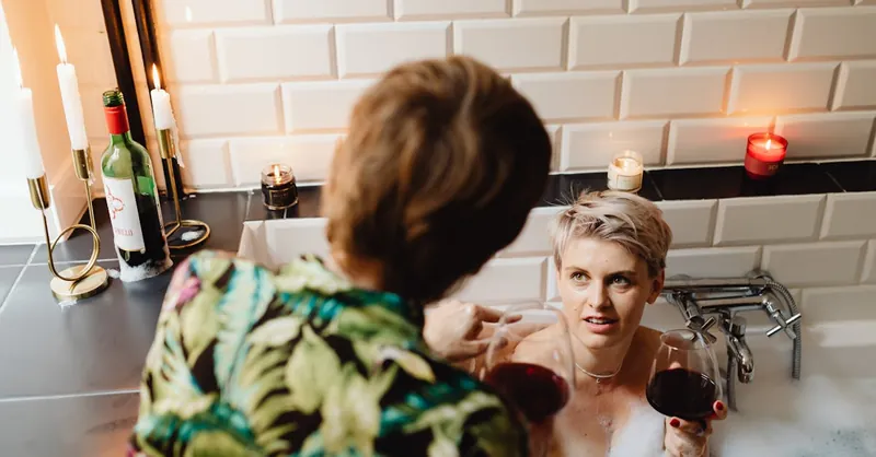 Couple enjoying a cozy and romantic bath with wine and candlelit ambiance.