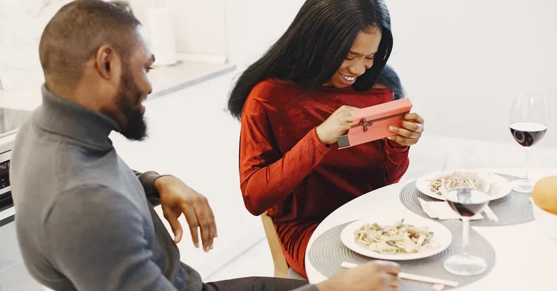 Happy couple enjoying a romantic dinner, exchanging gifts and savoring wine at home.