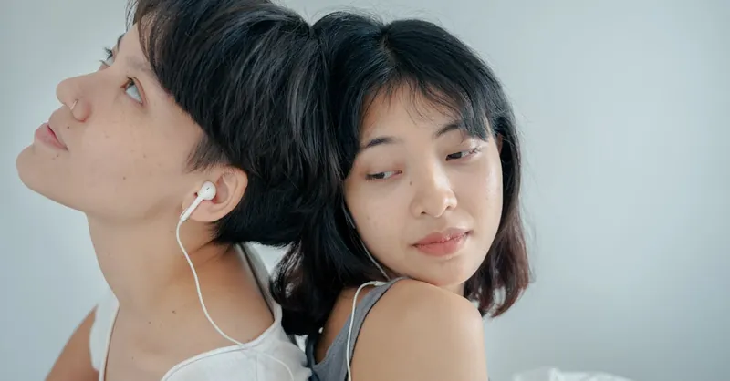 Close-up of a couple relaxing back to back with headphones indoors. Intimate and serene moment.