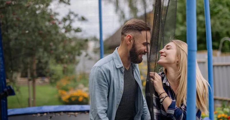 Smiling couple spending quality time together on an outdoor trampoline surrounded by nature.