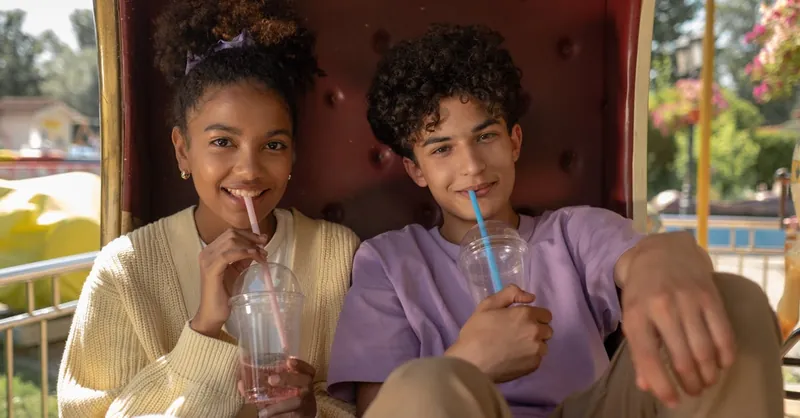 Smiling couple enjoying drinks on a sunny day at the amusement park. Perfect first date.