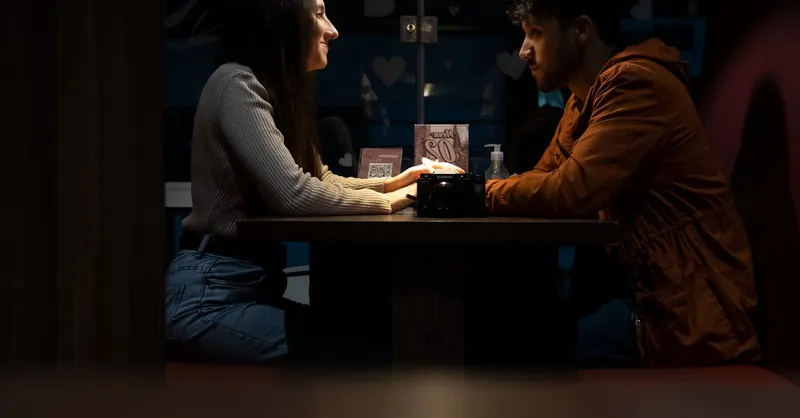 A couple sitting face-to-face, enjoying a romantic evening indoors with intimate lighting.