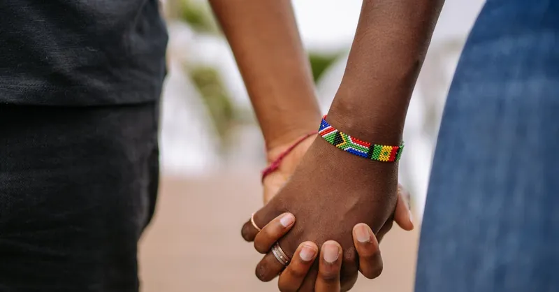 Close-up of diverse couple holding hands with colorful beaded bracelet emphasizing togetherness.