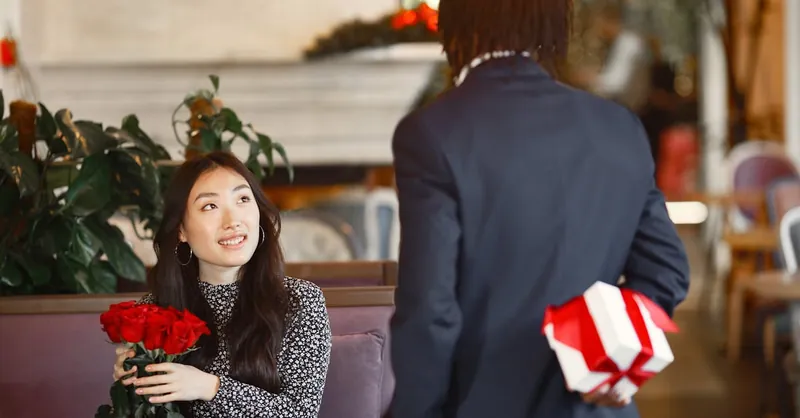 A romantic moment of surprise with roses and a gift in a cozy cafe scene.