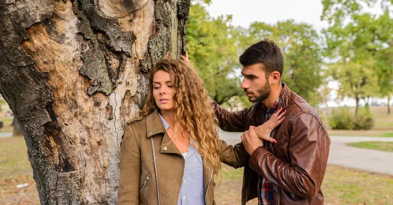 A man and a woman in an emotional conversation by a tree in a park.