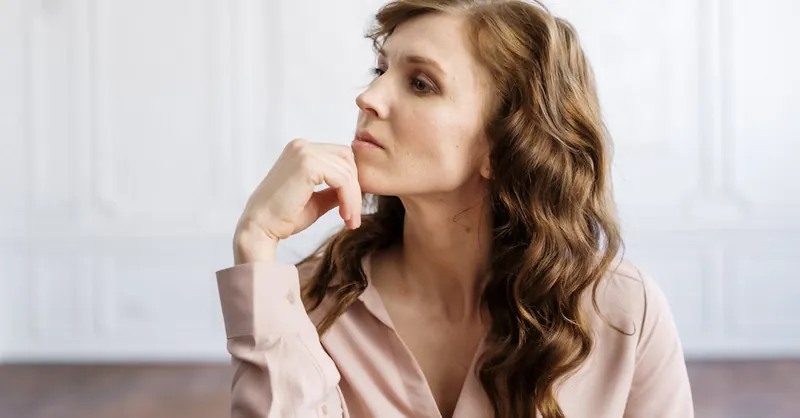 A thoughtful woman with curly hair sits indoors, reflecting deeply in a serene setting.
