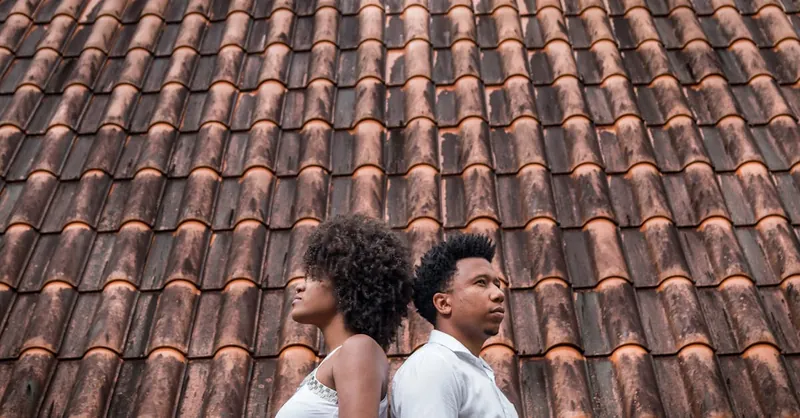Couple standing back to back against a rustic tiled roof, showcasing modern relationship dynamics.