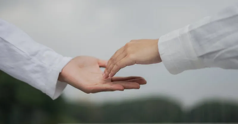 A symbolic image of two hands reaching out for connection and cooperation outdoors.