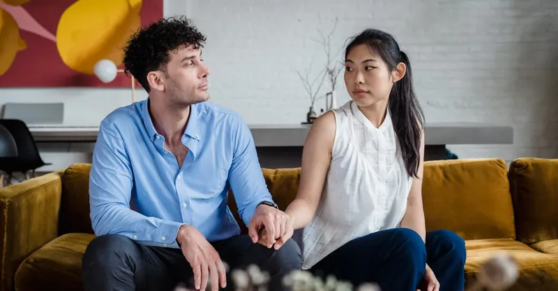 A couple sits on a sofa holding hands, showcasing intimacy and diversity indoors.
