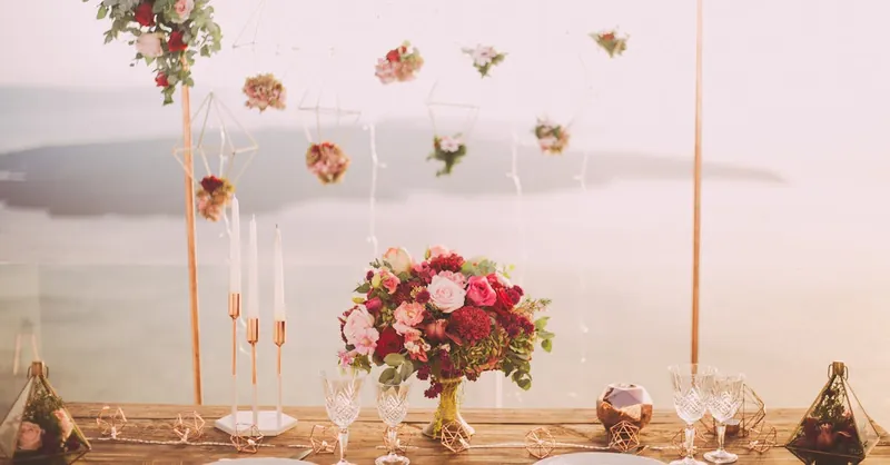 Romantic dining setup with flowers and candles overlooking Santorini waterscape at sunset.