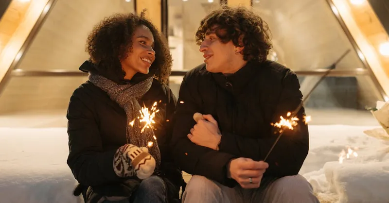A couple enjoying a romantic winter evening outdoors, sharing sparklers and smiles.