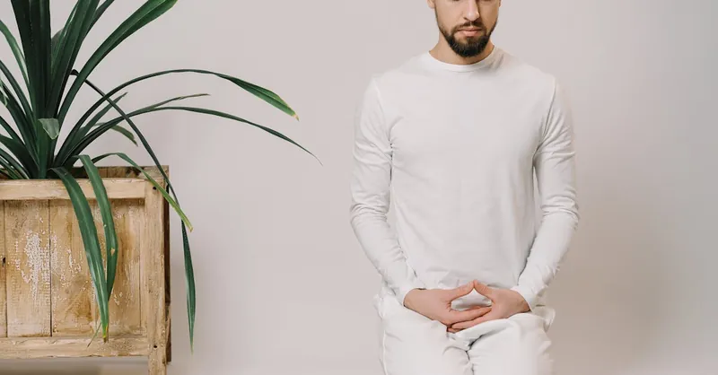A man meditates indoors in a minimalist setting, focusing on relaxation and mindfulness.