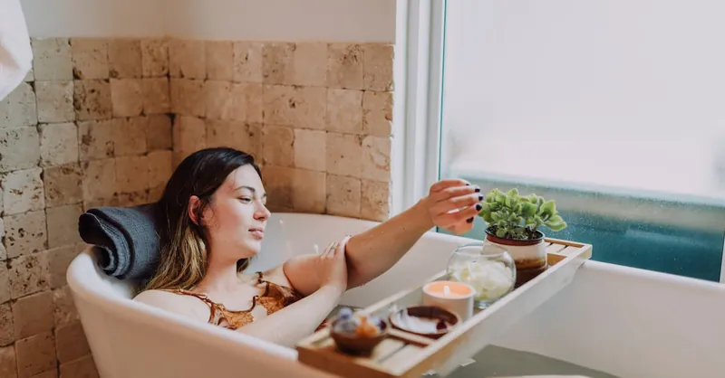 Woman enjoying a tranquil spa day with candles, flowers, and self-care rituals in a bathtub.