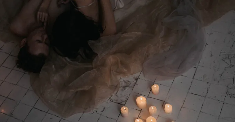 A couple embraces romantically on a rustic floor surrounded by candles, creating a warm atmosphere.