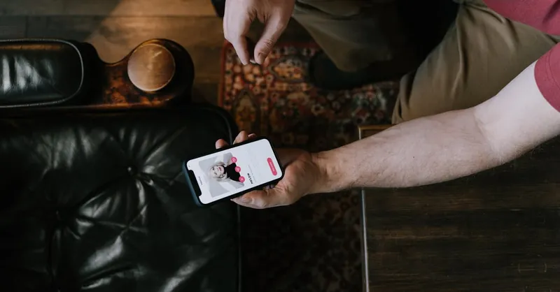 A person holding a smartphone with a dating app displayed while sitting on a leather chair.