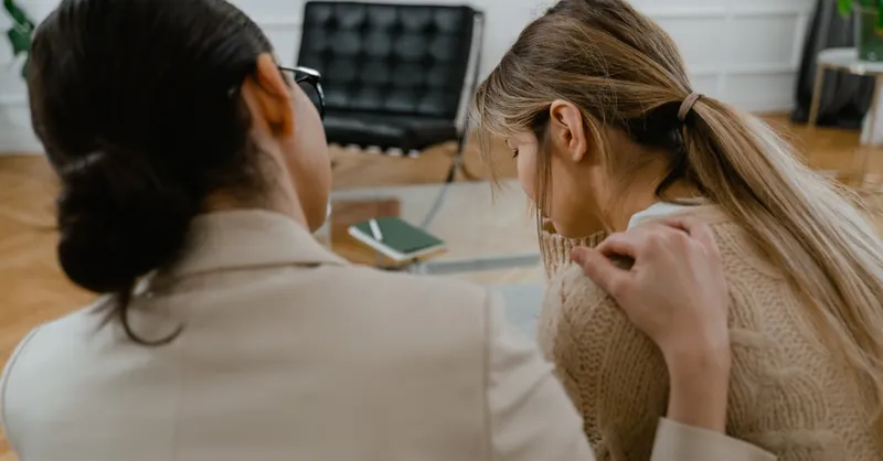 Two women sitting together, offering emotional support in a comforting setting.