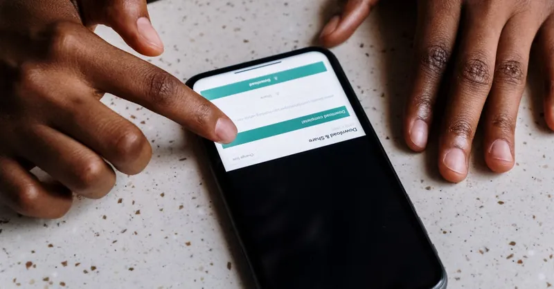 Close-up of hands interacting with a smartphone, displaying downloading interface.